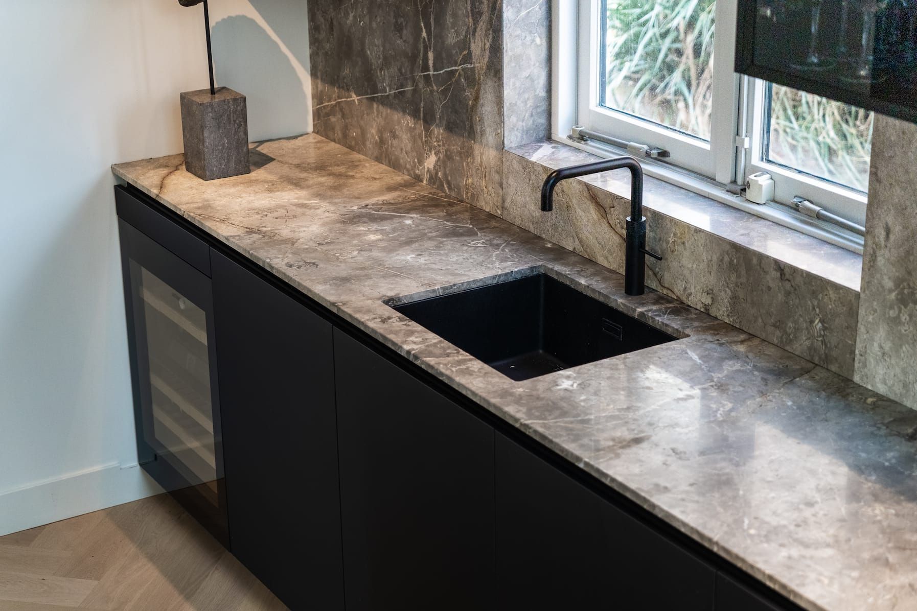 Stone worktop with black sink and tap beside a window in the kitchen