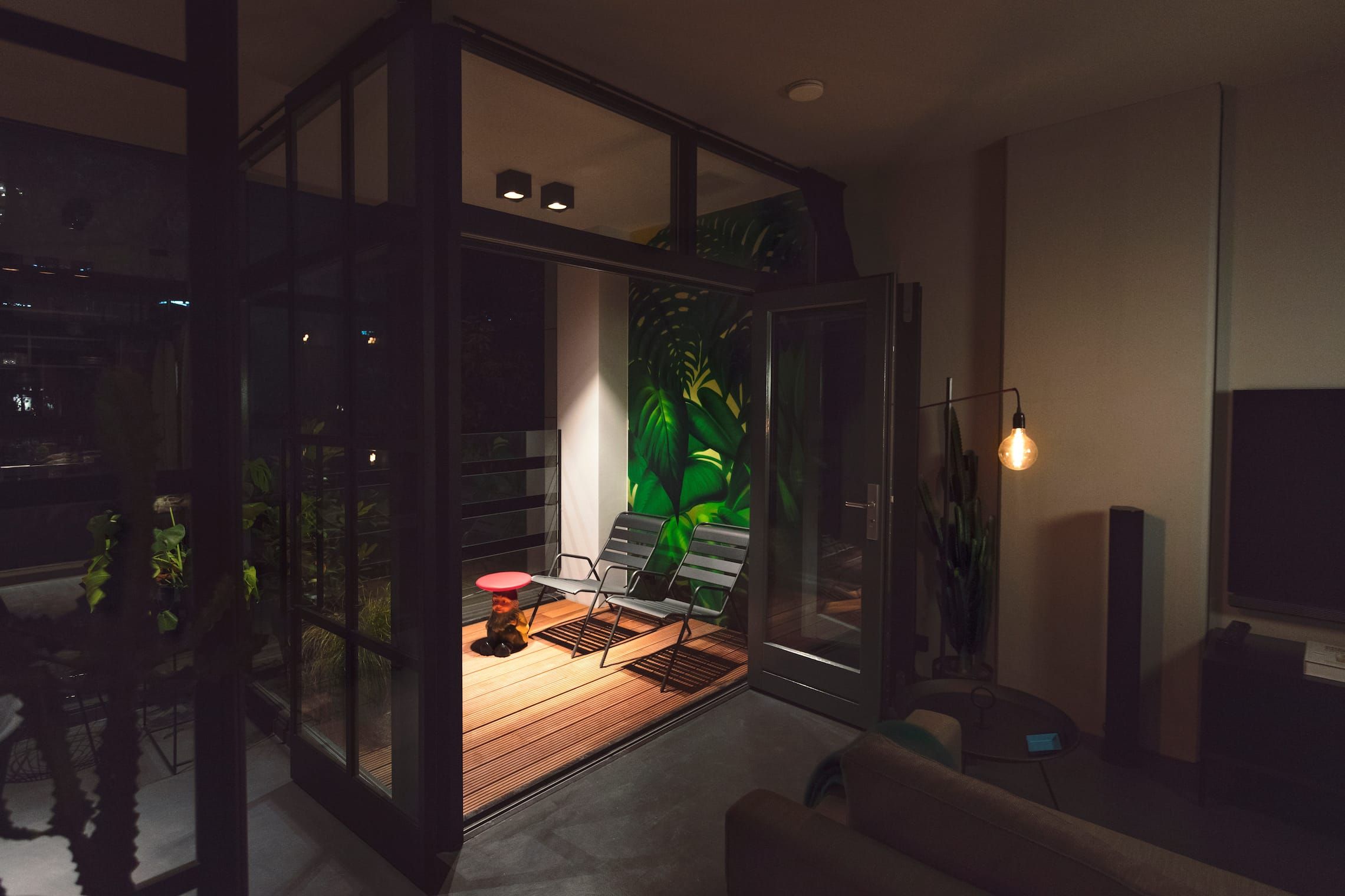 Balcony with timber deck and two chairs glowing beyond open glazed doors