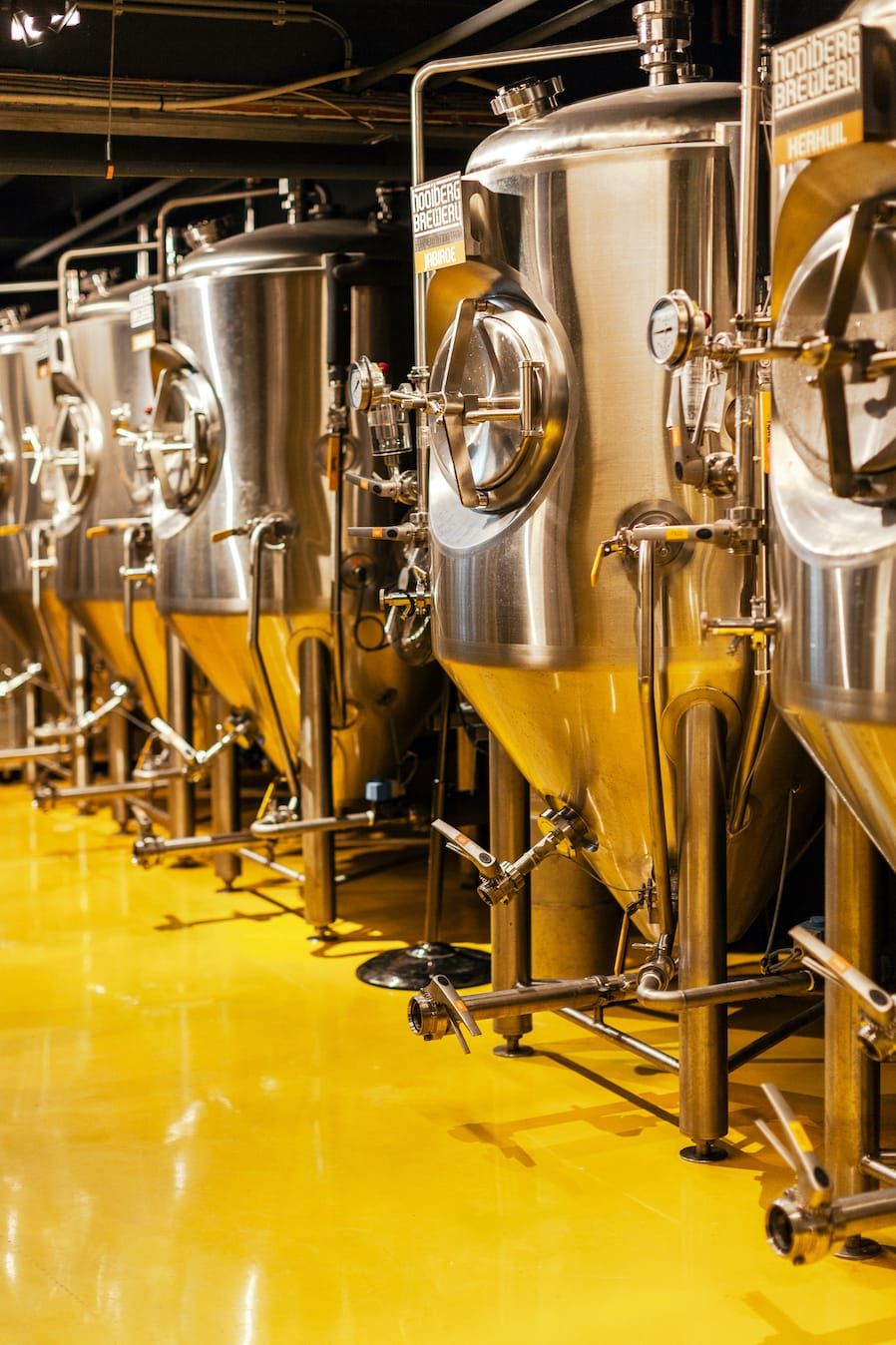 Stainless steel fermentation tanks on a bright yellow floor