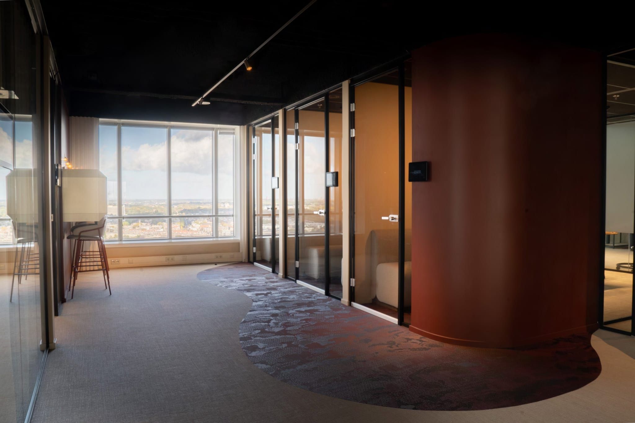 Corridor with glass meeting pods, a rust-coloured curved wall and patterned carpet