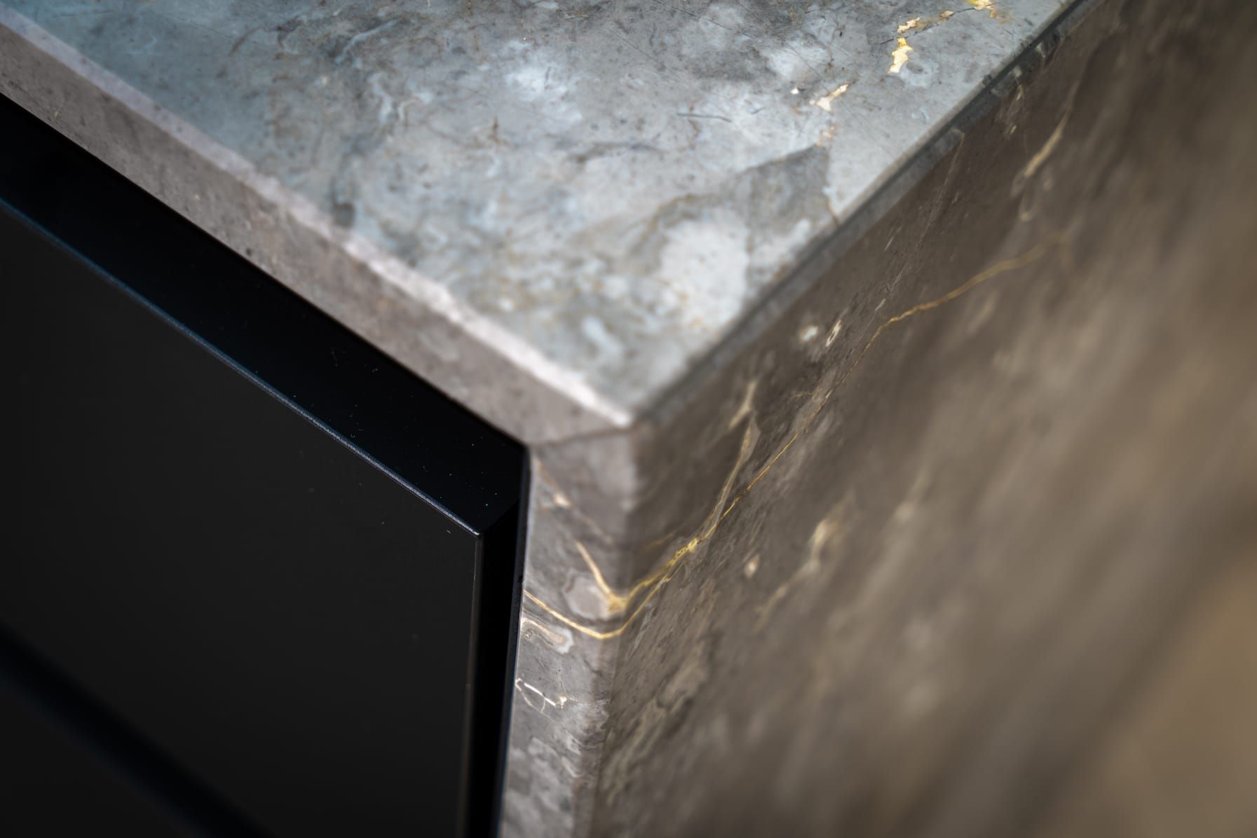 Veined stone worktop corner next to a matt black drawer front