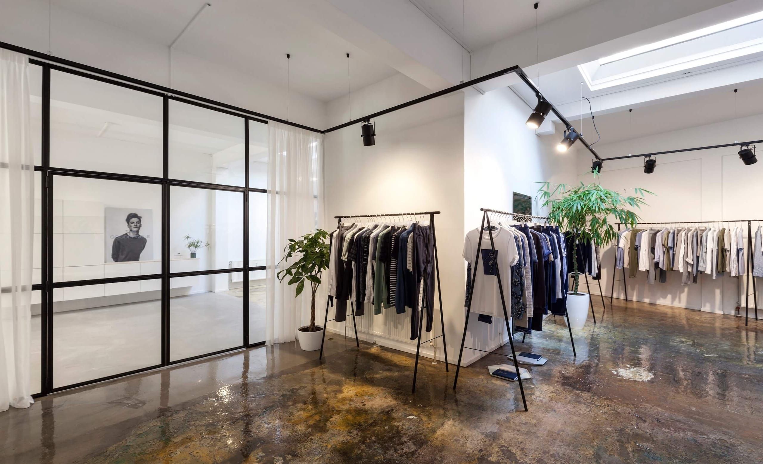 Clothing rails and potted plants beside a steel-framed glass partition with curtains