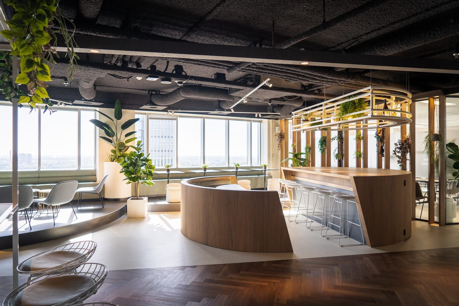 Open lounge with wooden bar, circular booth, wire stools and herringbone floor