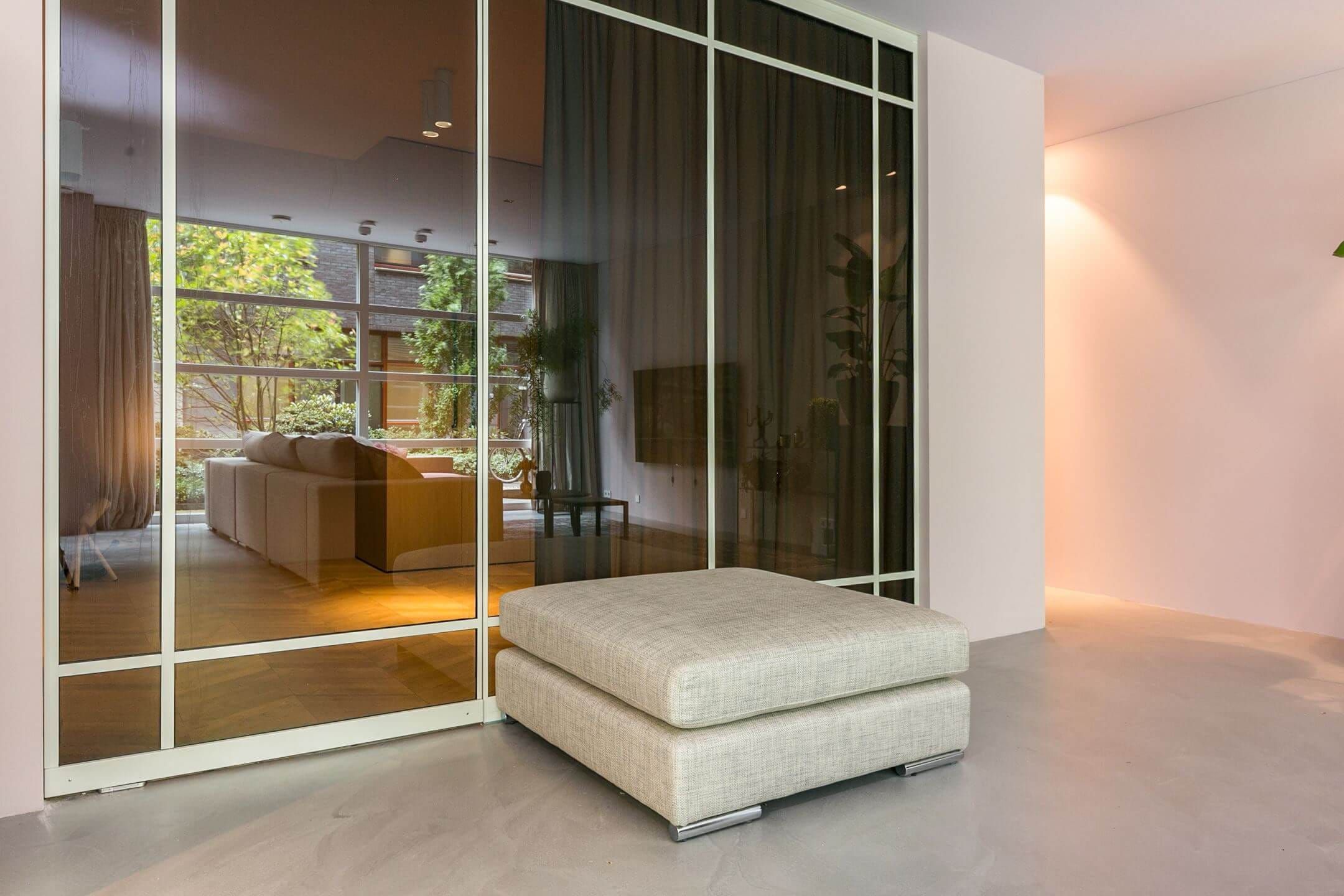 Cream ottoman beside a glass and steel partition looking into the living room