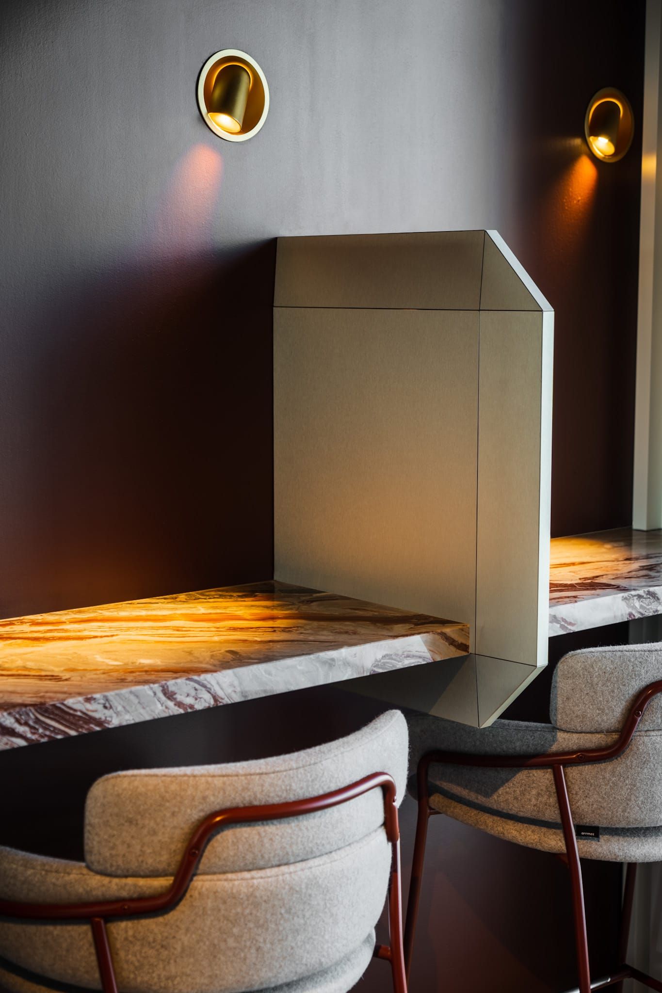Marble work counter with brass wall spotlights, a folded screen and upholstered stools