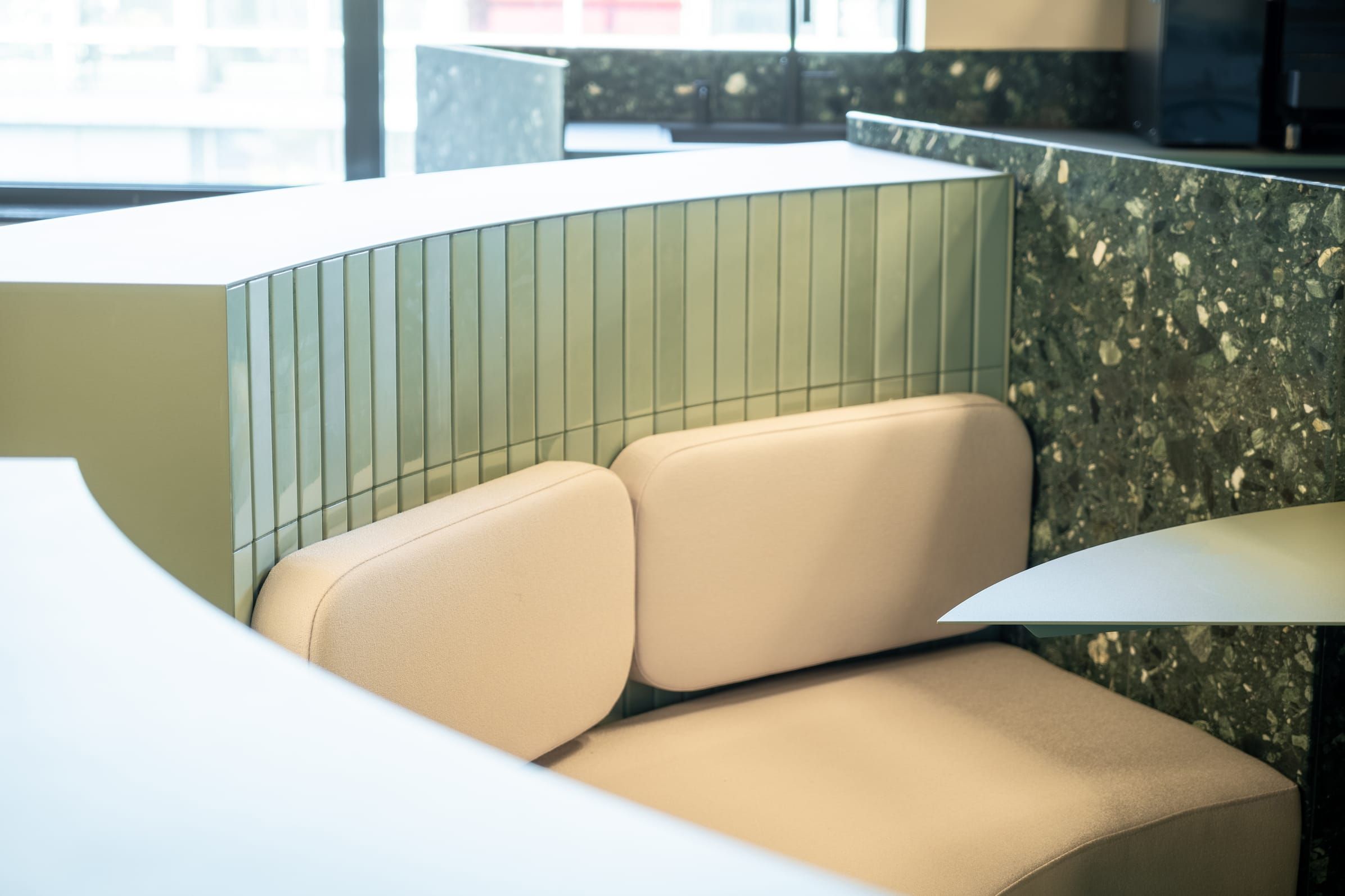 Beige cushioned booth seat against green tiles and a terrazzo wall