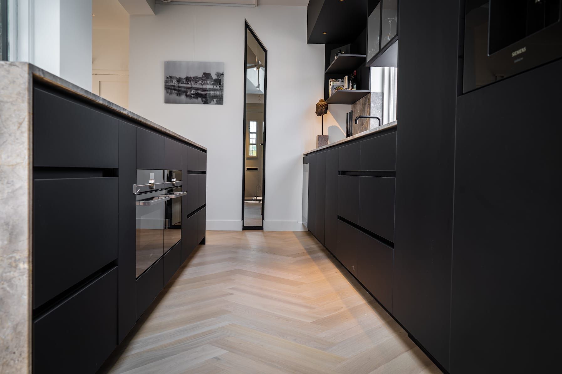 Low view along black kitchen units and herringbone floor to a steel framed door