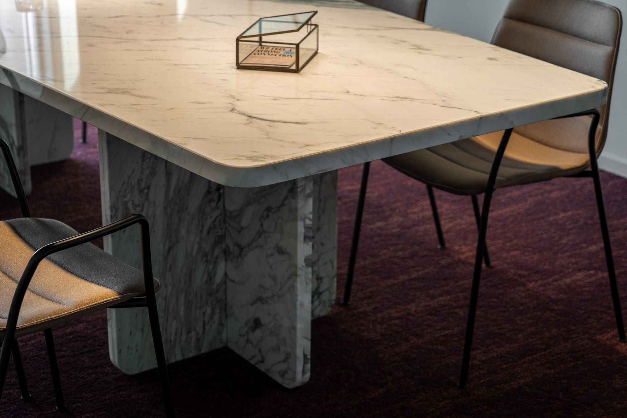 White marble table with stone base and black-framed chairs on plum carpet