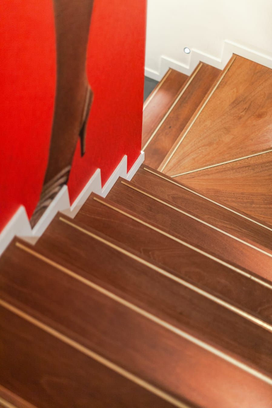 Wooden stair treads with brass inlays beside a red wall graphic