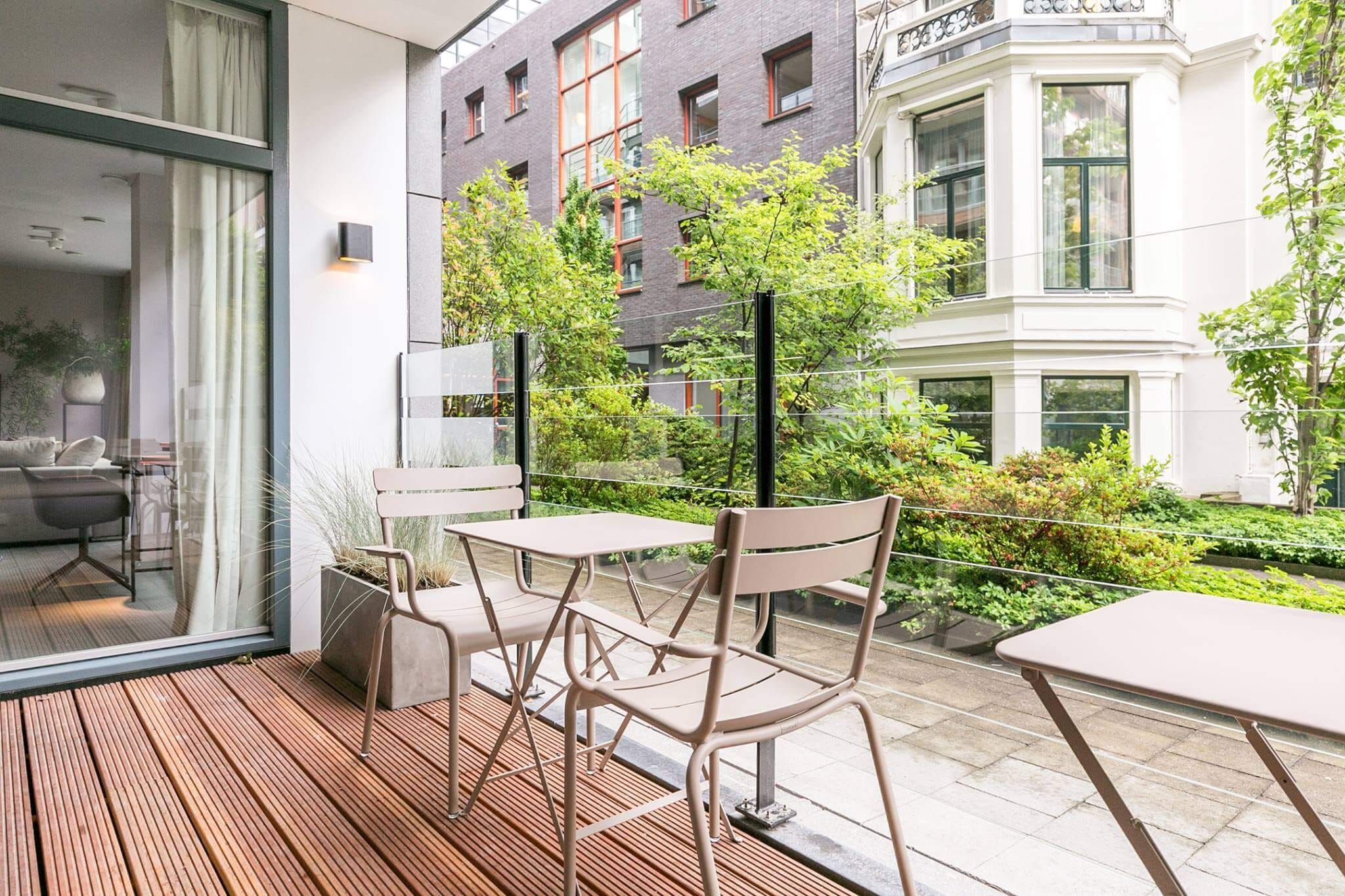 Terrace with wooden decking, bistro chairs and glass balustrade over a green courtyard