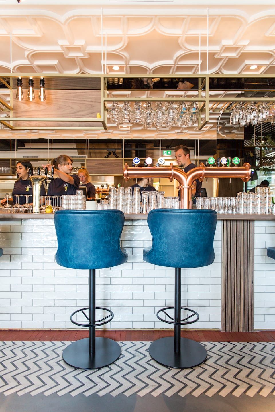 Bar with blue stools, copper tap tower and staff at De Gele Kanarie