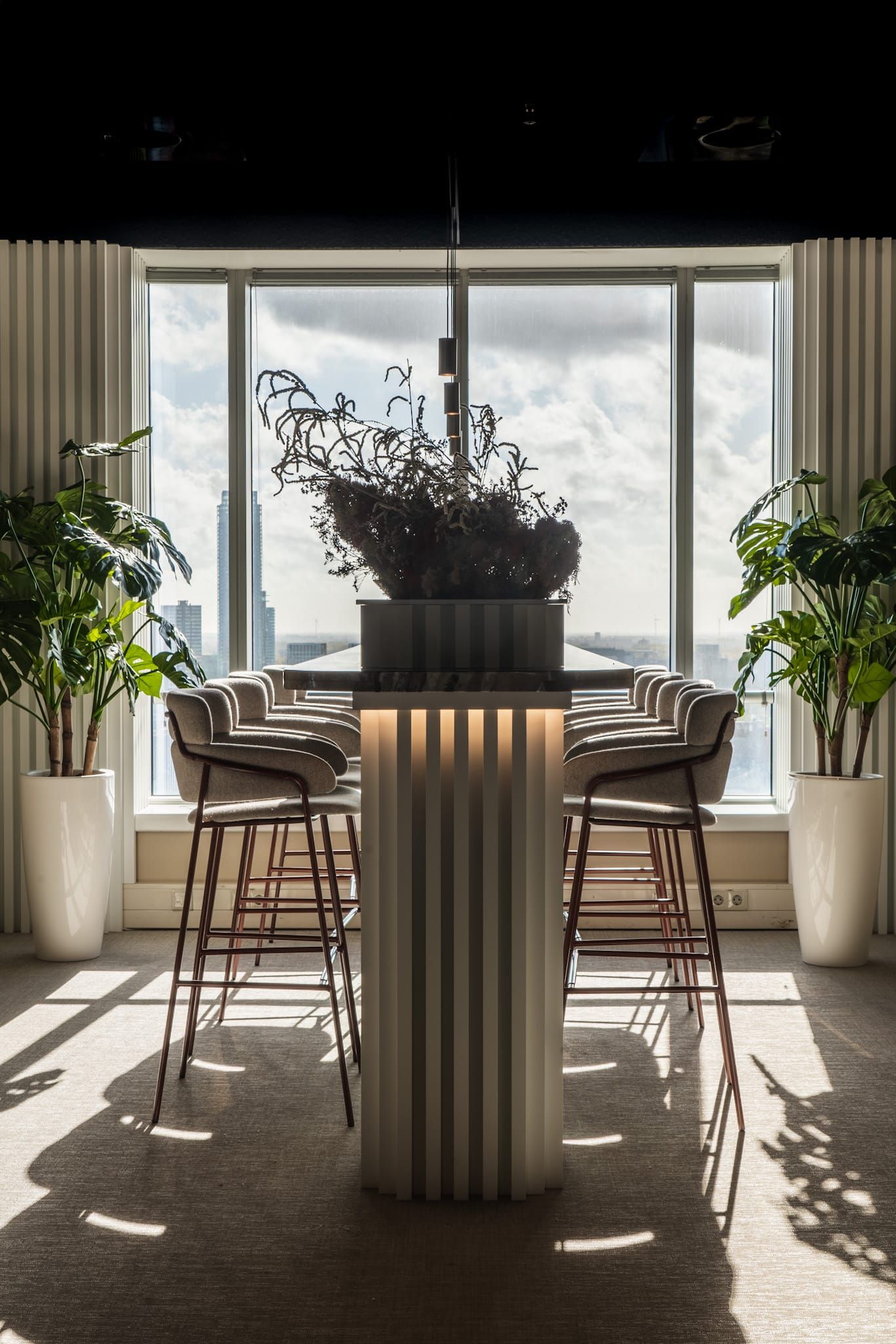 Tall fluted table with dried flowers and stools in front of a sunlit window