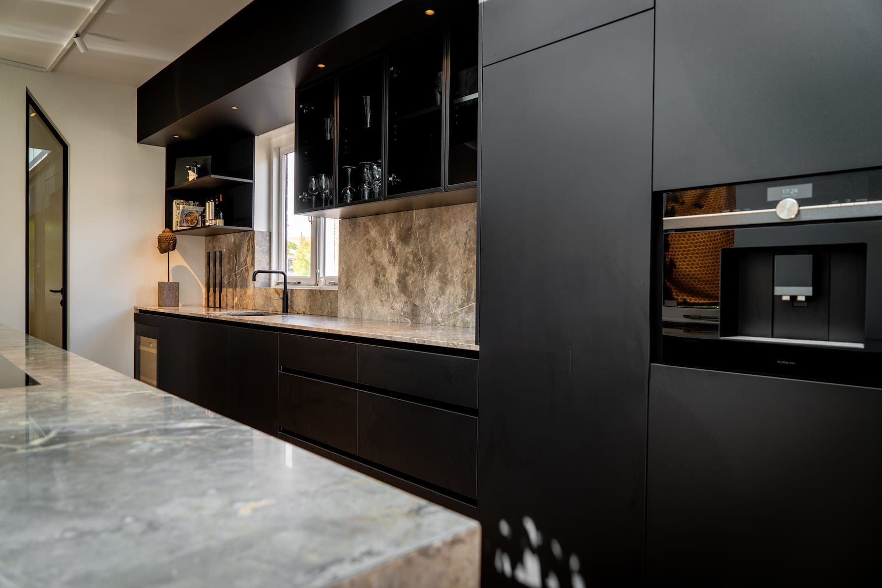Dark kitchen run with stone backsplash, glass cabinets and tall appliance units