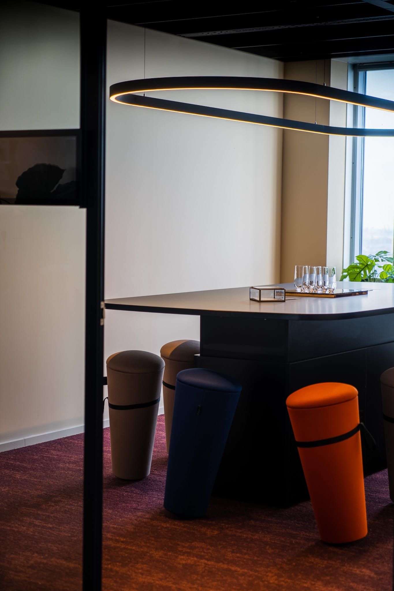 Standing table with colourful cone stools under a ring-shaped pendant light
