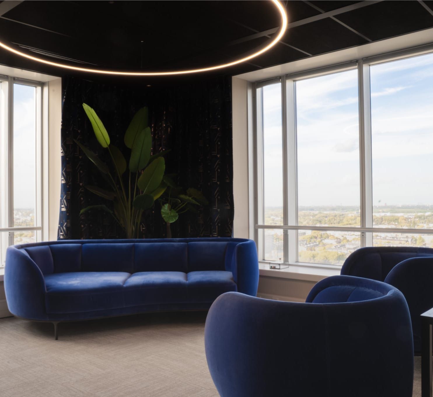 Blue velvet sofa and armchairs under a ring pendant with a city view