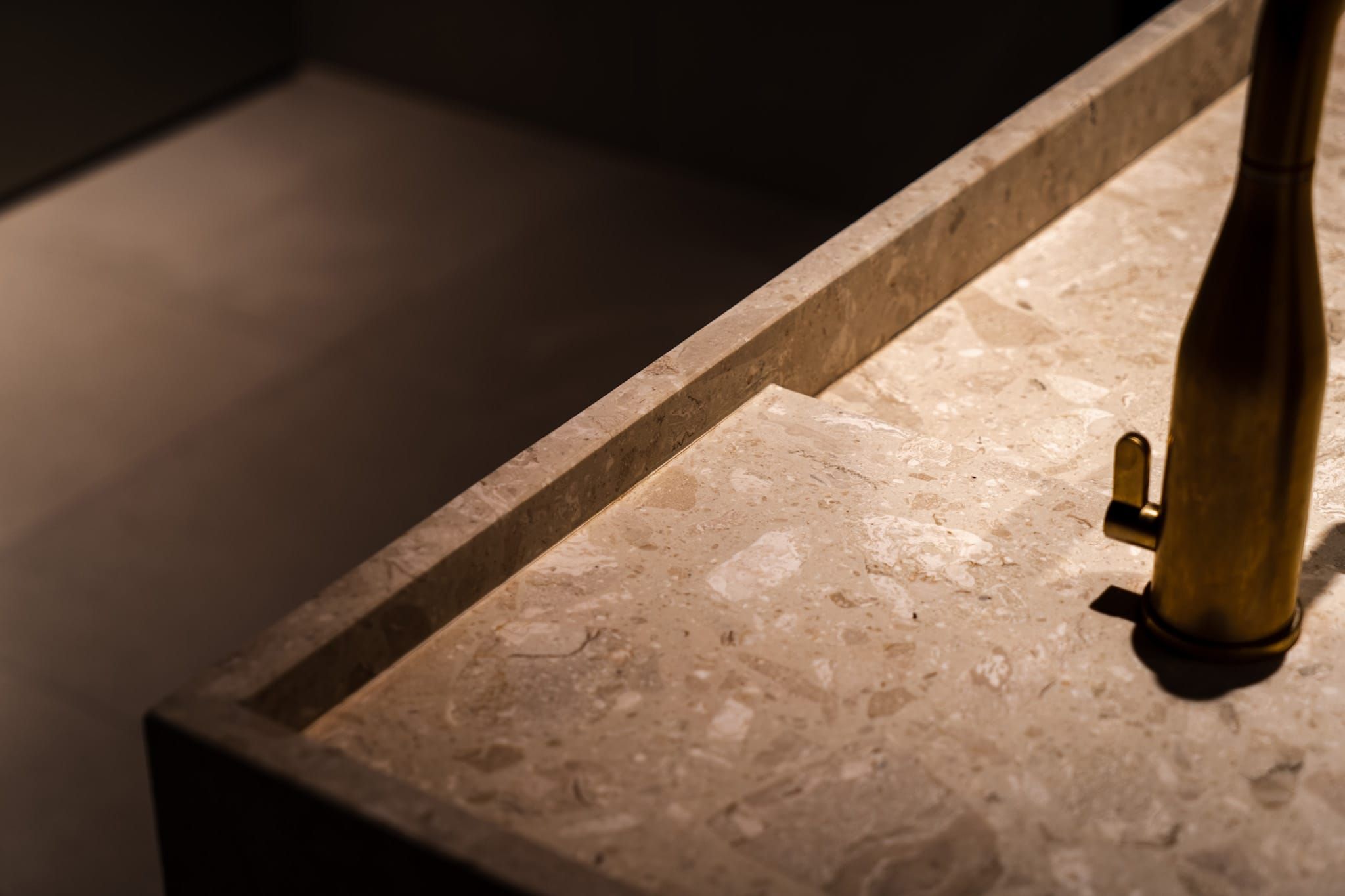 Close-up of a terrazzo basin with a brass tap in low light