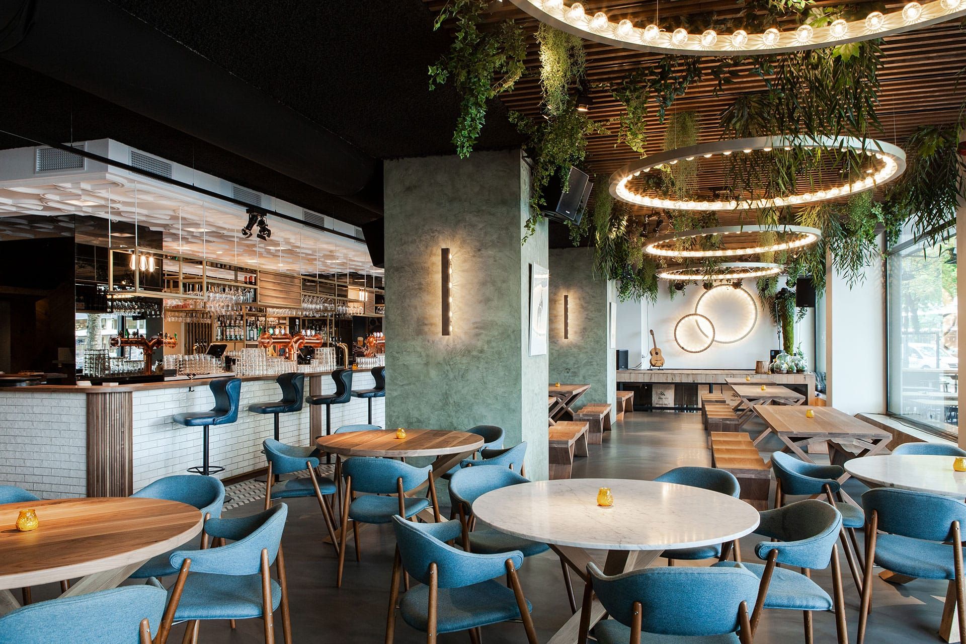 Restaurant with blue chairs, round wooden tables and a long bar